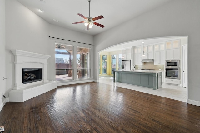 unfurnished living room featuring visible vents, a fireplace with raised hearth, ceiling fan, a sink, and light wood-type flooring