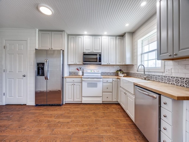 kitchen with backsplash, butcher block countertops, appliances with stainless steel finishes, wood finished floors, and a sink