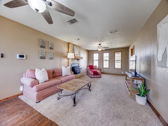 living area featuring visible vents, baseboards, a stone fireplace, and wood finished floors