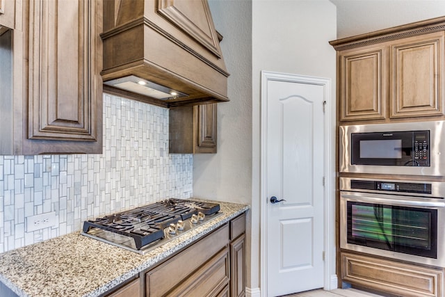 kitchen featuring decorative backsplash, light stone countertops, appliances with stainless steel finishes, and custom range hood