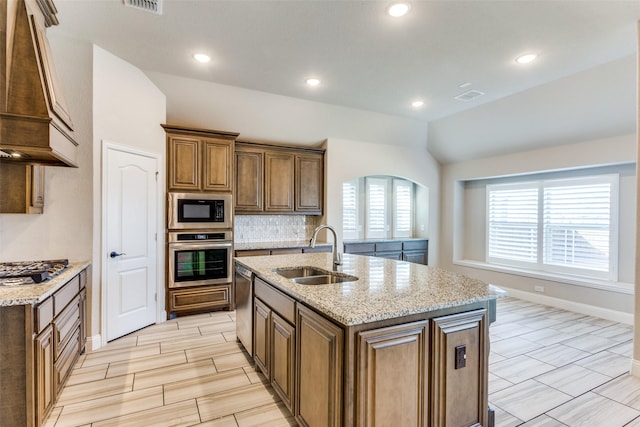 kitchen featuring a center island with sink, custom range hood, vaulted ceiling, stainless steel appliances, and a sink