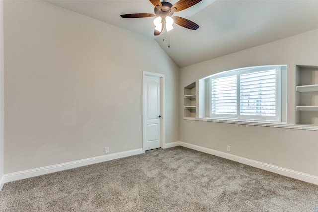 carpeted spare room with baseboards, built in shelves, a ceiling fan, and lofted ceiling