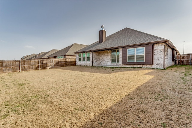 back of property with a lawn, a fenced backyard, a shingled roof, brick siding, and a chimney