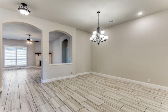 empty room featuring a fireplace, ceiling fan with notable chandelier, visible vents, and baseboards