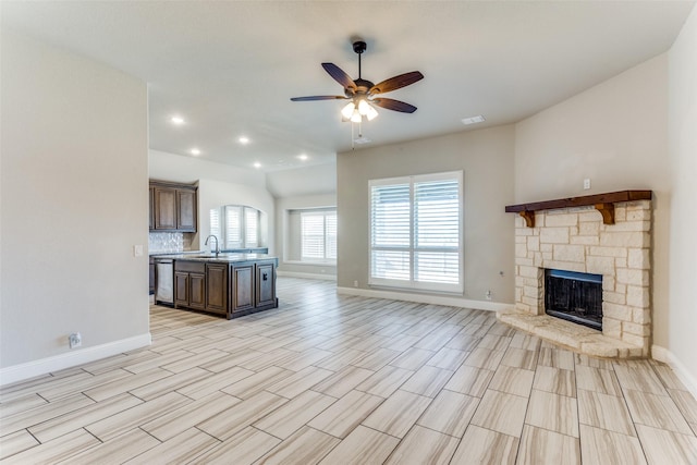 kitchen featuring ceiling fan, open floor plan, light countertops, a stone fireplace, and a sink