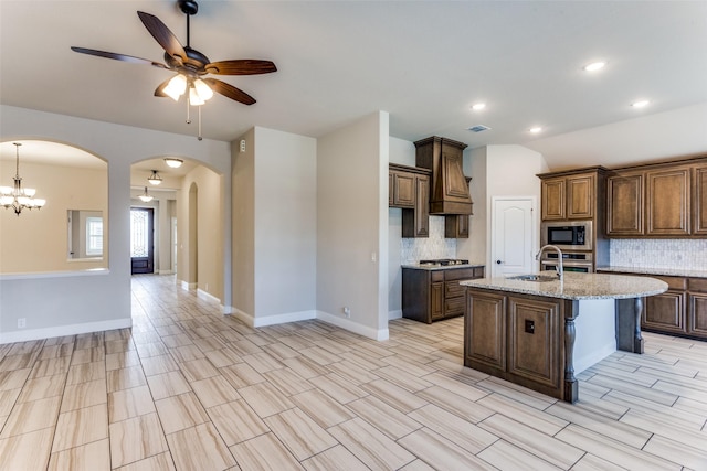 kitchen with backsplash, custom range hood, ceiling fan with notable chandelier, appliances with stainless steel finishes, and arched walkways