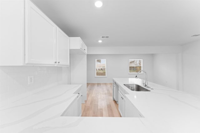 kitchen with light stone counters, a sink, decorative backsplash, white cabinets, and light wood-type flooring