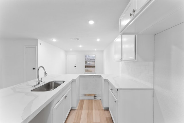 kitchen featuring a sink, light stone countertops, light wood-style floors, and white cabinetry