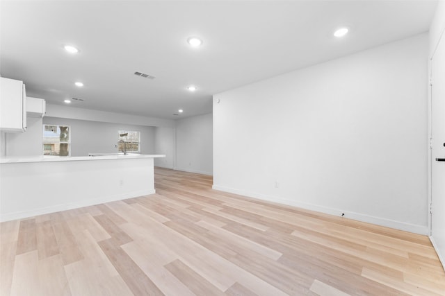 unfurnished living room featuring visible vents, a sink, recessed lighting, light wood-style floors, and baseboards