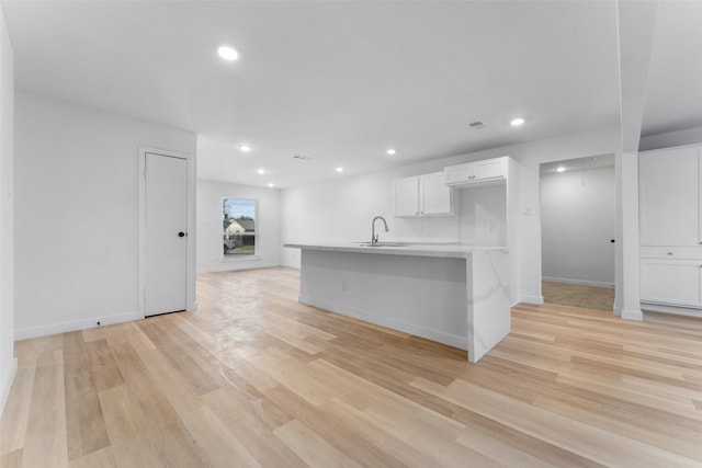 kitchen featuring light wood-style flooring, white cabinetry, light countertops, and a sink