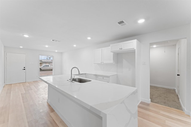 kitchen featuring visible vents, white cabinetry, light wood-type flooring, and a sink