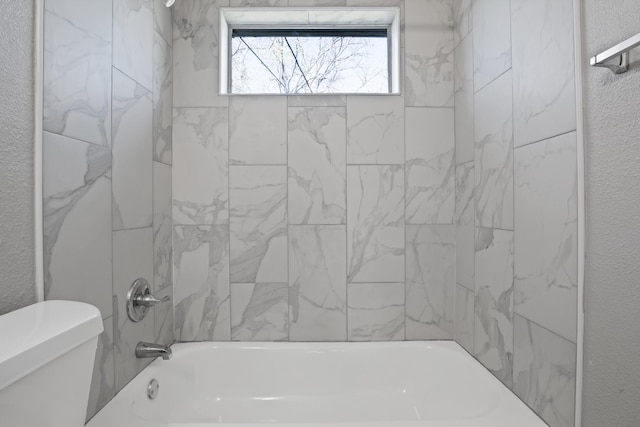 bathroom with toilet, a textured wall, and shower / bathtub combination