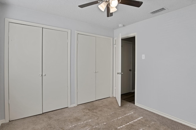 unfurnished bedroom with carpet, visible vents, two closets, and a textured ceiling