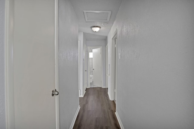 hallway featuring visible vents, attic access, dark wood-type flooring, and baseboards