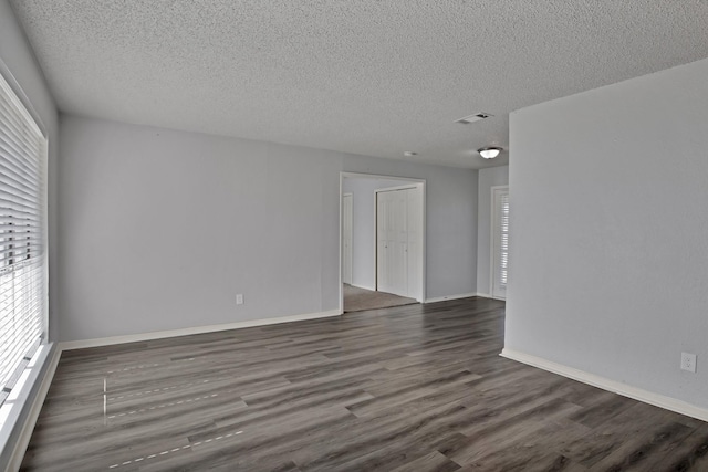 unfurnished room with visible vents, a textured ceiling, and dark wood-style floors