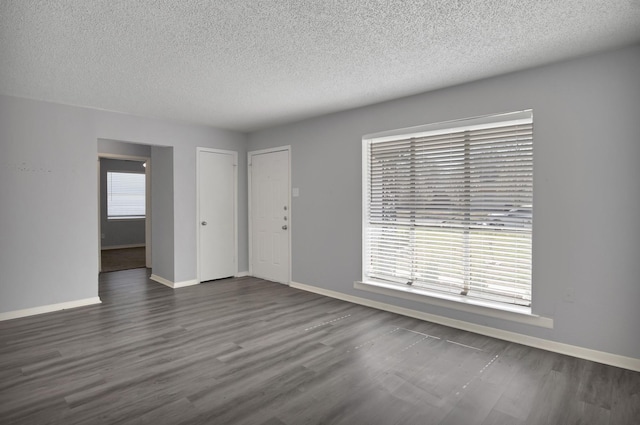 empty room with baseboards, dark wood-type flooring, and a textured ceiling