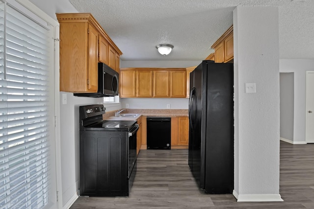 kitchen with light wood finished floors, black appliances, baseboards, a textured ceiling, and a sink