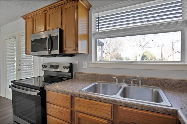 kitchen with brown cabinetry, a textured ceiling, stainless steel appliances, and a sink