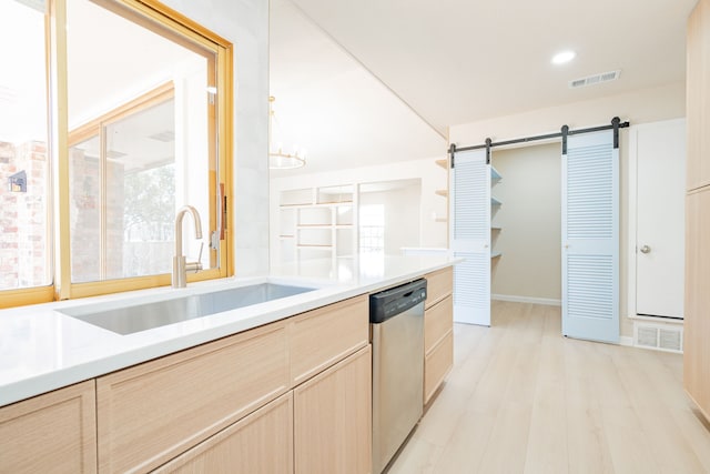 kitchen with visible vents, light brown cabinets, a barn door, stainless steel dishwasher, and a sink