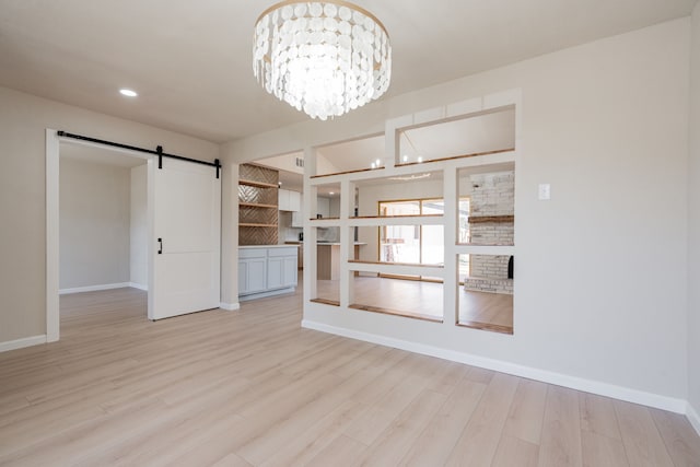 spare room featuring baseboards, recessed lighting, a barn door, light wood-type flooring, and a chandelier