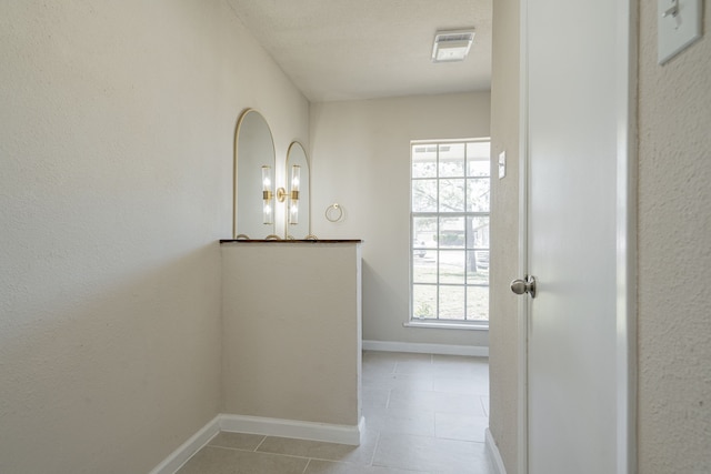 hallway featuring tile patterned floors, visible vents, and baseboards