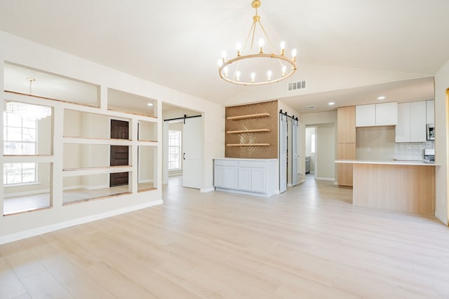 unfurnished living room featuring visible vents, lofted ceiling, light wood-style floors, a barn door, and a notable chandelier