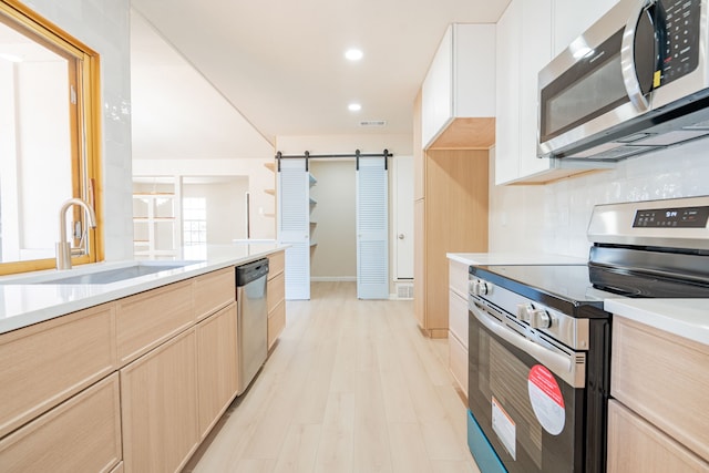 kitchen with light brown cabinets, light countertops, a barn door, appliances with stainless steel finishes, and a sink