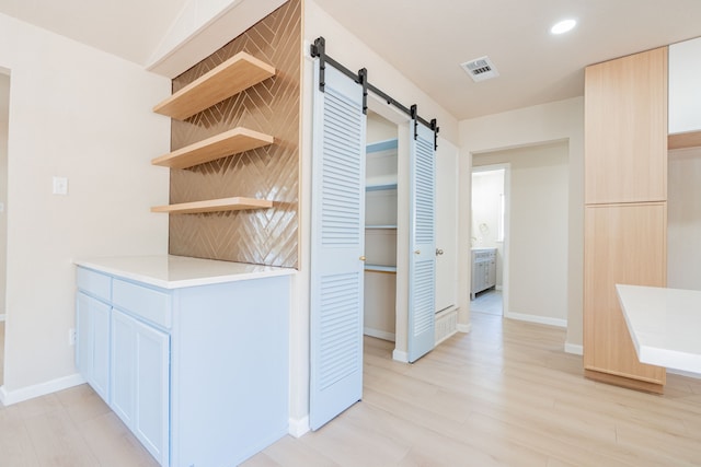 hall with visible vents, baseboards, recessed lighting, light wood-style floors, and a barn door