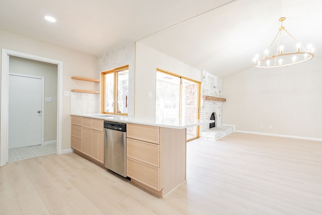 kitchen featuring light brown cabinets, open floor plan, a fireplace, stainless steel dishwasher, and a sink