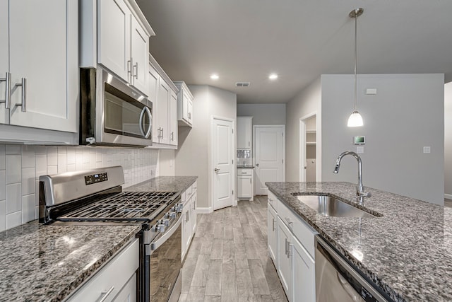 kitchen featuring dark stone countertops, visible vents, a sink, stainless steel appliances, and light wood-style floors