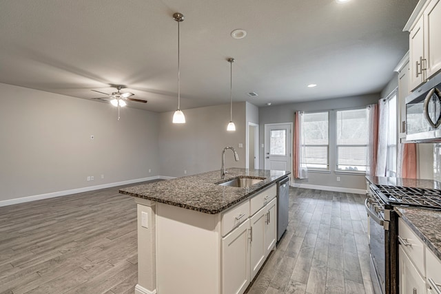 kitchen featuring baseboards, dark stone counters, a sink, appliances with stainless steel finishes, and light wood-type flooring