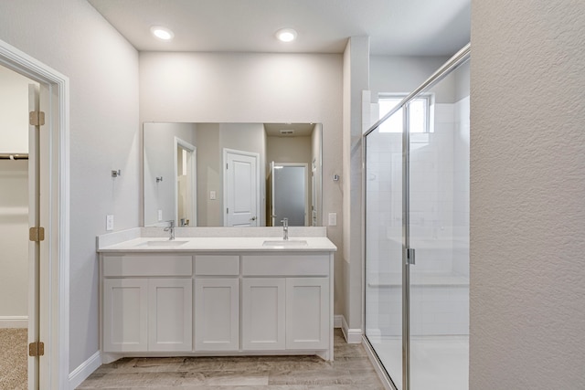 full bath with double vanity, a shower stall, wood finished floors, and a sink