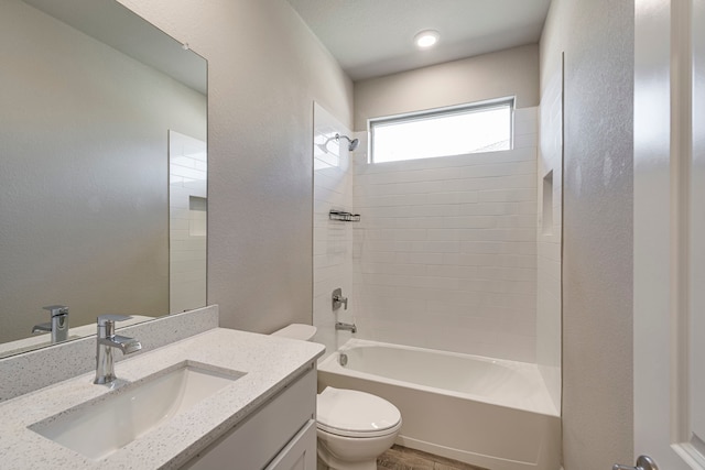 bathroom featuring toilet, vanity, a textured wall, and washtub / shower combination