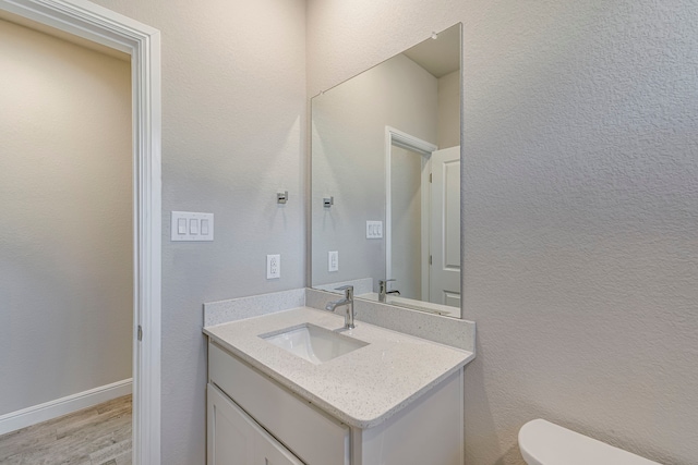 bathroom with vanity, wood finished floors, baseboards, toilet, and a textured wall