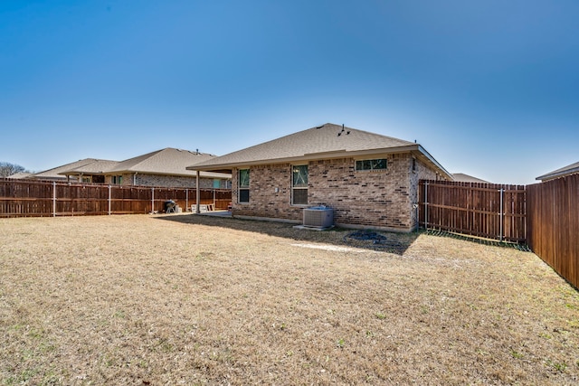 rear view of property featuring cooling unit, a fenced backyard, brick siding, and a lawn