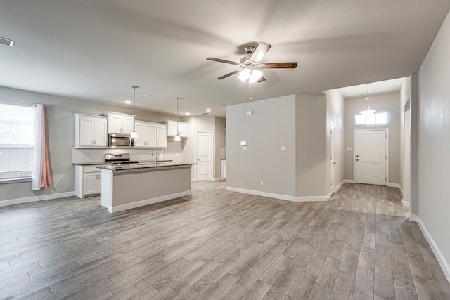 kitchen with light wood-type flooring, stainless steel appliances, white cabinetry, open floor plan, and a wealth of natural light