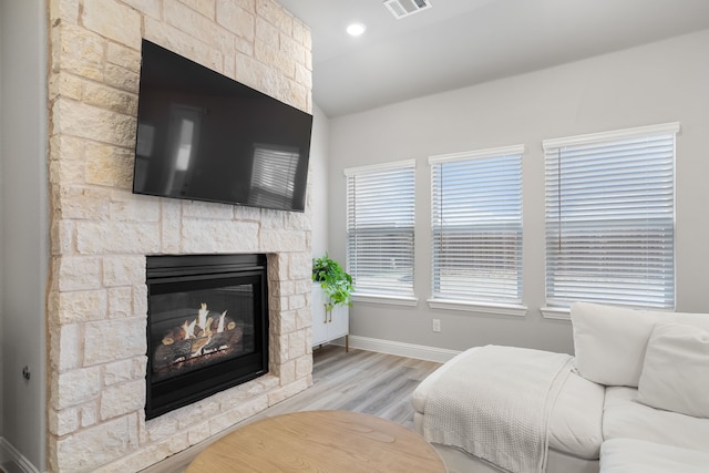 living area with visible vents, baseboards, lofted ceiling, a stone fireplace, and wood finished floors