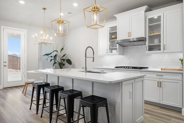 kitchen with backsplash, under cabinet range hood, light countertops, gas stovetop, and a sink