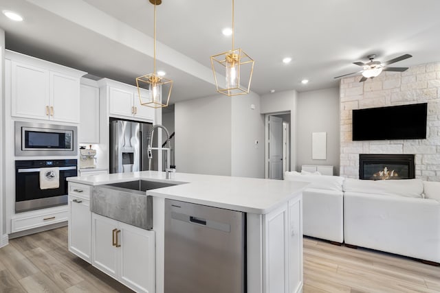 kitchen featuring light wood-type flooring, a kitchen island with sink, open floor plan, appliances with stainless steel finishes, and light countertops