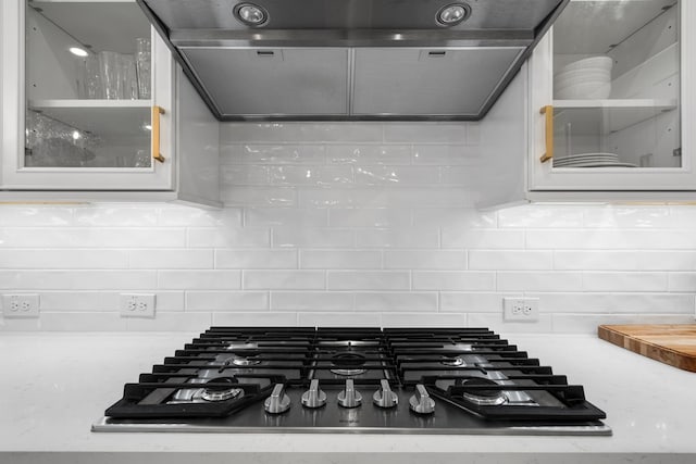 details featuring light countertops, ventilation hood, glass insert cabinets, and stainless steel gas stovetop