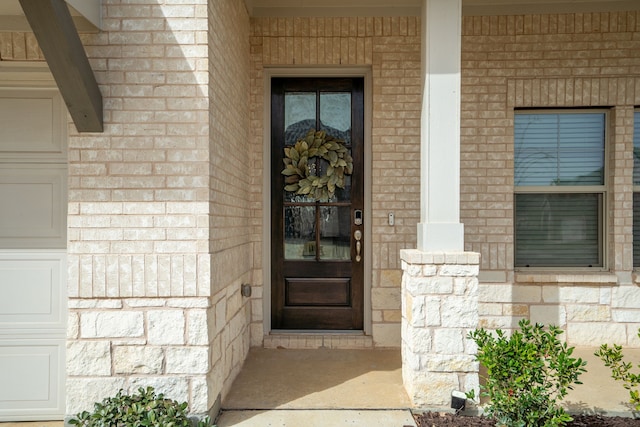 view of exterior entry featuring an attached garage, brick siding, and stone siding