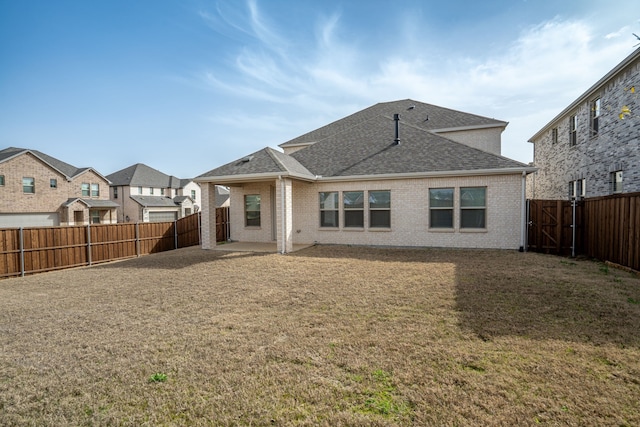 rear view of house with a lawn, a fenced backyard, brick siding, and a shingled roof