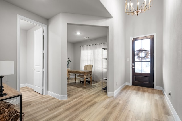 foyer entrance featuring baseboards, light wood-type flooring, and a chandelier