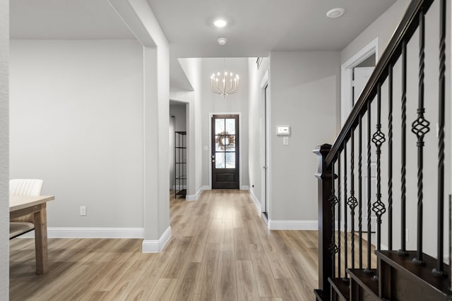 foyer entrance featuring a chandelier, stairway, light wood-style flooring, and baseboards