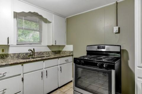 kitchen with light tile patterned floors, stone countertops, a sink, white cabinets, and gas range oven