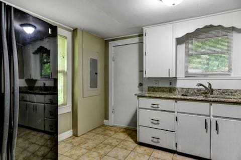 kitchen with a sink, electric panel, white cabinetry, stone counters, and baseboards