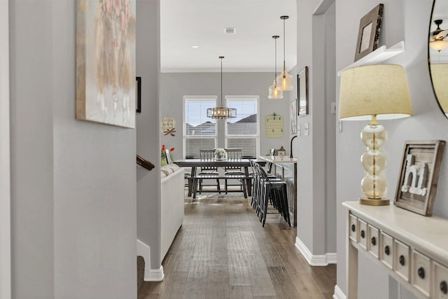 hall with visible vents, baseboards, ornamental molding, a notable chandelier, and dark wood-style flooring