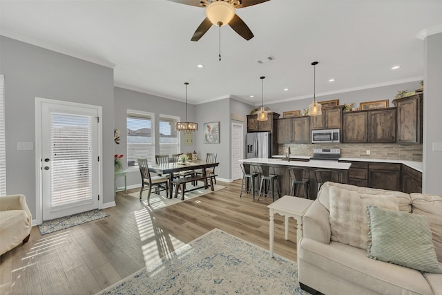 living room with visible vents, baseboards, light wood-style flooring, and ceiling fan with notable chandelier