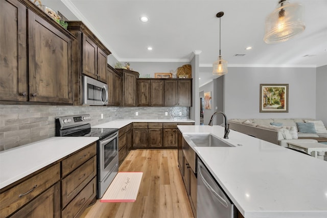 kitchen with a sink, open floor plan, light wood-type flooring, appliances with stainless steel finishes, and a kitchen island with sink