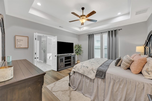 bedroom featuring visible vents, ornamental molding, light wood-style floors, a raised ceiling, and a ceiling fan